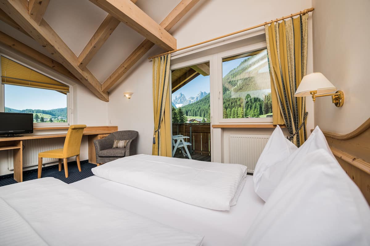 Ein Hotelzimmer mit Bett, Schreibtisch, Stuhl, Fernseher und einem Fenster mit Vorhängen.