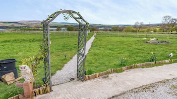 A rural landscape with a wooden archway, a gravel path, and a fenced field.