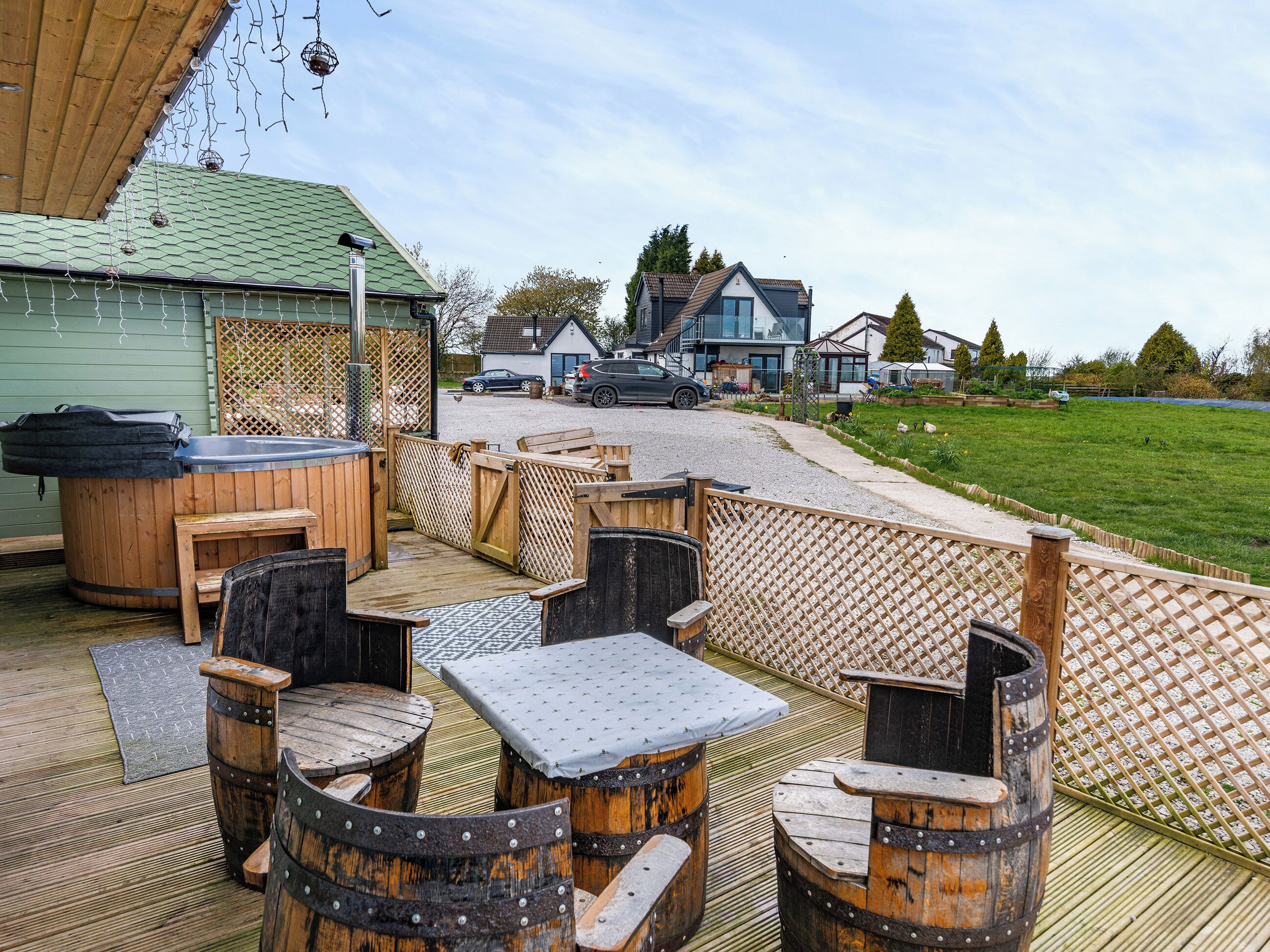 Un patio al aire libre con mobiliario de madera, incluyendo mesas y sillas, y un jacuzzi.