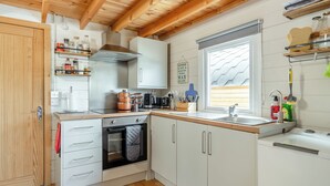 A compact kitchen with wooden beams, white cabinets, a built-in oven, and a window with blinds. - 2 bedroom accommodation in Altham (Altham)