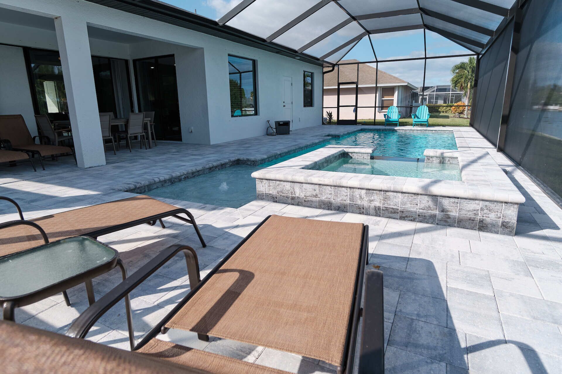 A covered outdoor swimming pool area with lounge chairs and a patio table.