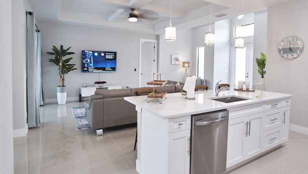 A modern kitchen with a central island, stainless steel dishwasher, and white cabinetry. - Waterfront home with pool and spa close to shopping (Cape Coral)