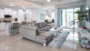 A modern living room with a sofa, a coffee table, and a dining area with a table and chairs. There is a kitchen area with cabinets and appliances. - Waterfront home with pool and spa close to shopping (Cape Coral)