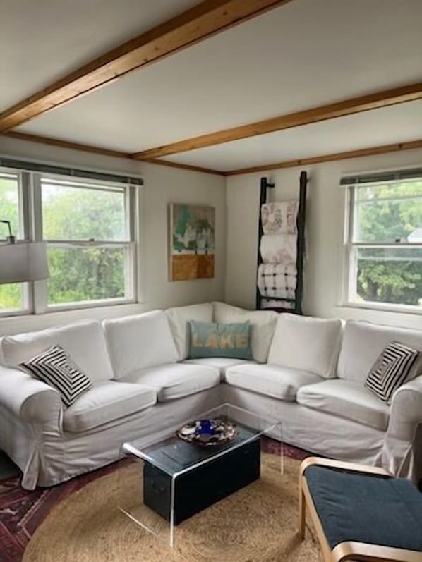 Una sala de estar en esquina con un sofá sectional blanco, una mesa de centro negra y una ventana con vista a árboles.