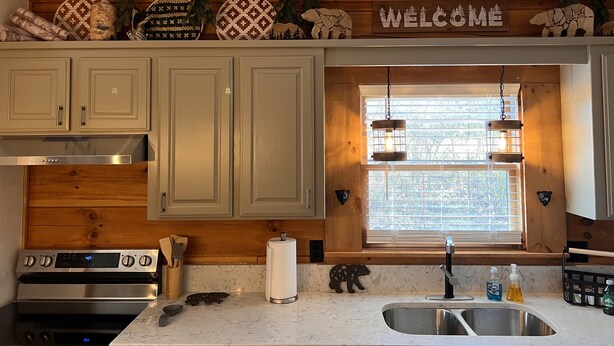 A kitchen with wooden cabinets, a stainless steel oven, a window with a view, and a 'Welcome' sign above the window. - Bear Cabin - Close to Magic Springs, Off-Road Park (Hot Springs)