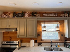 Une cuisine avec des meubles en bois, un four en acier inoxydable, une fenêtre avec vue et une pancarte « Bienvenue » au-dessus de la fenêtre.