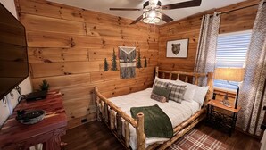 A wooden cabin bedroom with a bed, a desk, a ceiling fan, and a window with curtains. - Bear Cabin - Close to Magic Springs, Off-Road Park (Hot Springs)
