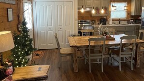 A cozy living room with a wooden floor, a dining table with chairs, a Christmas tree, and a leather couch. - Bear Cabin - Close to Magic Springs, Off-Road Park (Hot Springs)