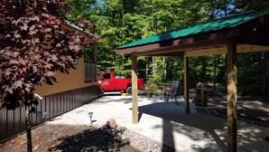 Un espacio al aire libre techado con un camión rojo estacionado cerca, rodeado de árboles y una estructura de madera.