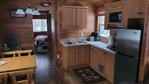 Cocina estilo cabaña con armarios de madera, un refrigerador de acero inoxidable, un fregadero y una zona de comedor con mesa y sillas de madera.