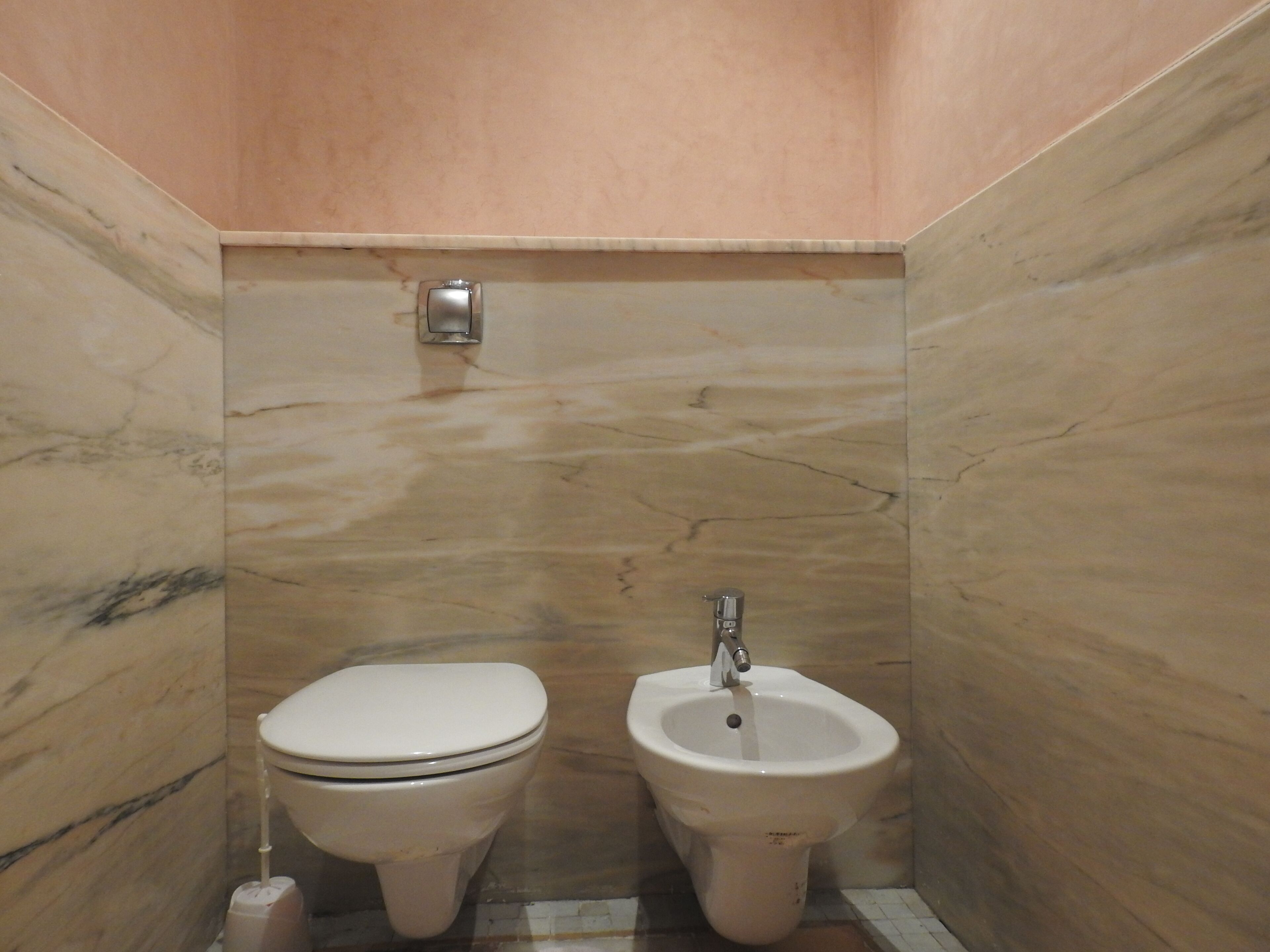 Une petite salle de bain avec des toilettes et un bidet, des murs en marbre et un sol carrelé.