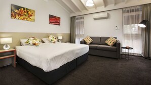 A hotel room with a large bed, a sofa, a nightstand with a lamp, and a window with curtains. - Nightcap at the Ranch Hotel (Sydney)