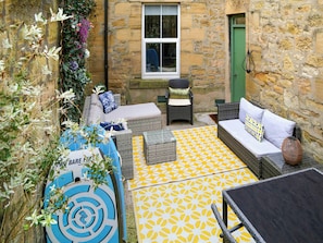 A cozy outdoor seating area with wicker furniture, a yellow patterned rug, and a stone wall backdrop.