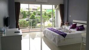 A hotel room with a balcony, a bed with white bedding and purple pillows, a desk with a computer, and a TV on the wall. - Pandora House Pattaya (Pattaya)