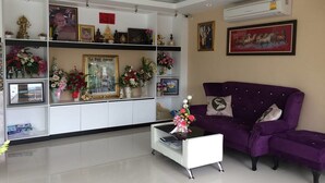 A living room with a purple sofa, a white coffee table, and shelves with various items including flowers and framed pictures. - Pandora House Pattaya (Pattaya)