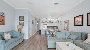 A spacious living room with a light blue sofa, a white coffee table, and a dining area with a chandelier.