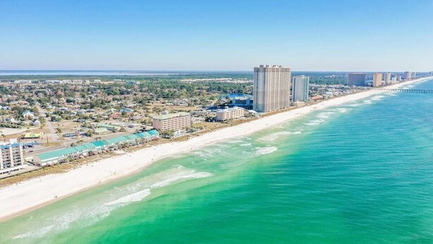 An aerial view of a coastal area with a beach, a large hotel, and a bridge in the distance.