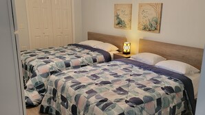 A bedroom with two beds, each with a patterned bedspread, a nightstand with a lamp, and two wall art pieces above the beds.