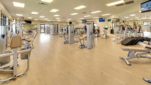 Un gimnasio amplio con diversas máquinas de ejercicio, espejos y una pantalla de televisión.