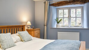 Une chambre à coucher avec un lit en bois, une table de chevet avec une lampe, une fenêtre avec des rideaux et un radiateur.