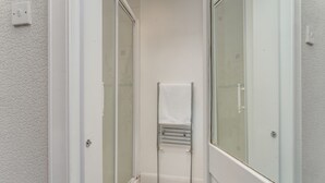 Een smalle badkamer met een douchecabine van glas, een handdoekhouder en een witte handdoek op de vloer.