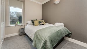 Een slaapkamer met een bed, nachtkastje, raam en een wandlamp.