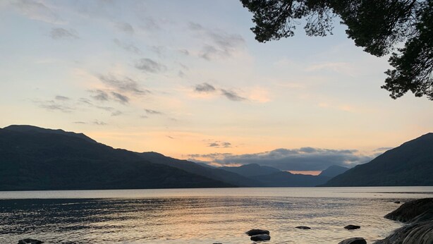 Een natuurlandschap met een meer, bergen en een rotsachtige kustlijn.