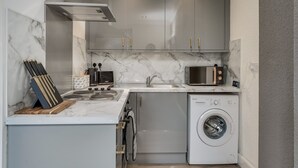 Een compacte keuken met een ingebouwde wasmachine, een magnetron en een roestvrijstalen afzuigkap.