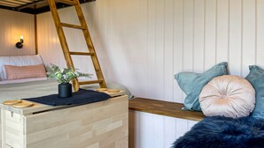 A cozy bedroom with a wooden bed, a ladder, a small plant, and a furry object.