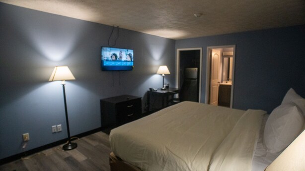 Un dormitorio con cama, dos lámparas de noche, televisor en la pared, cómoda y puerta que da a otra habitación.