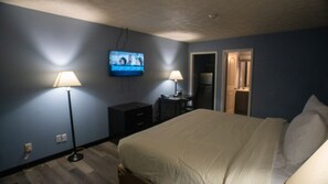 Un dormitorio con cama, dos lámparas de noche, televisor en la pared, cómoda y puerta que da a otra habitación.