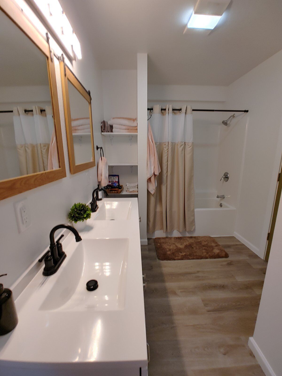 A modern bathroom with a double sink, a large mirror, a shower with a curtain, and a small rug on the floor.