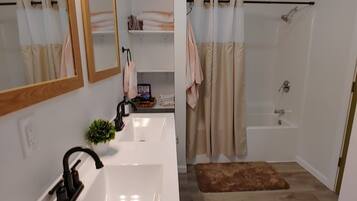 A modern bathroom with a double sink, a large mirror, a shower with a curtain, and a small rug on the floor.