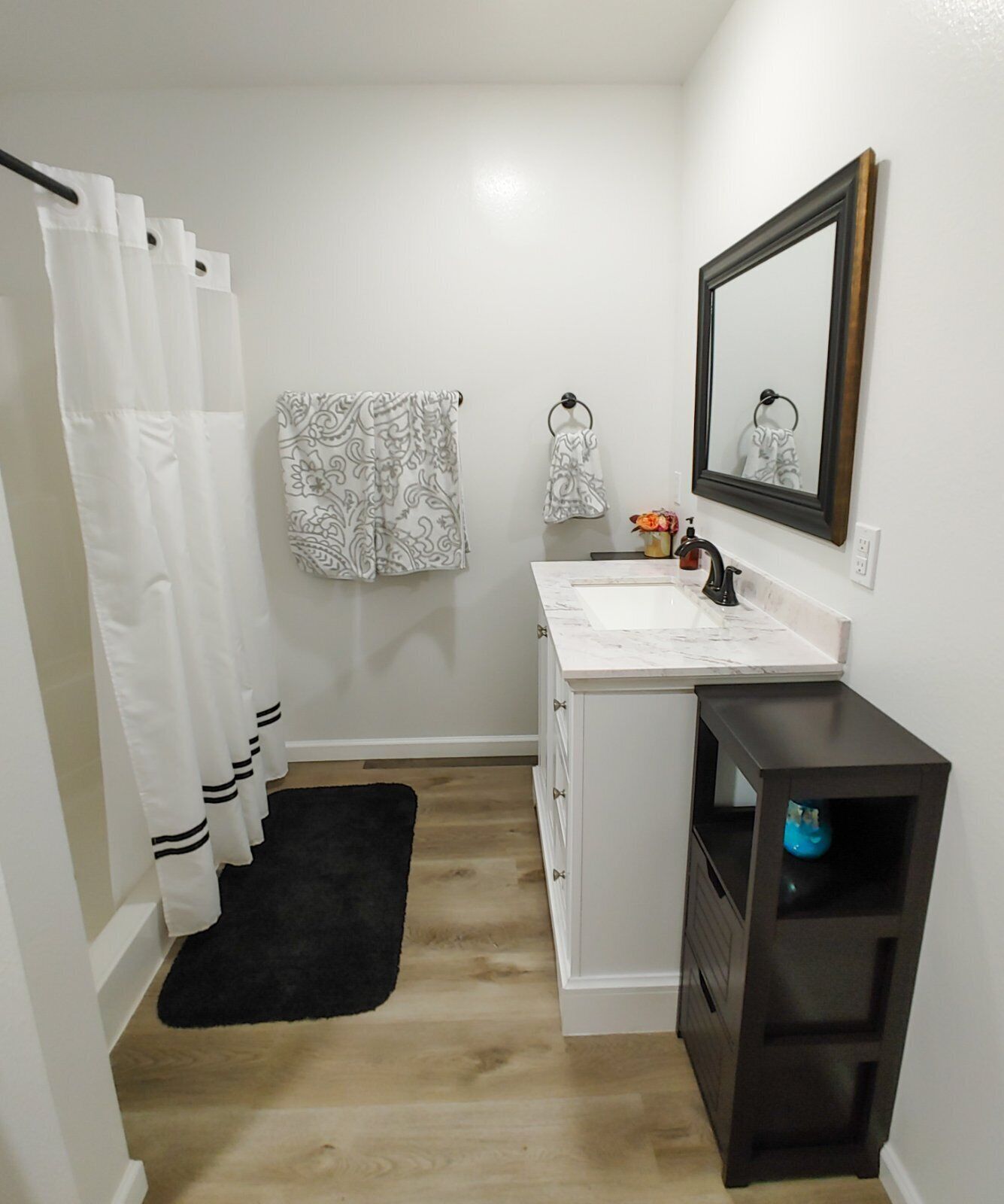 A bathroom with a white vanity, a black shelf, a mirror, and a shower curtain.