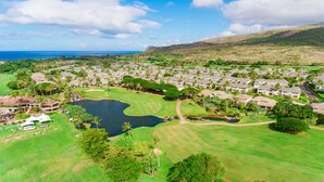 A golf course with a pond, surrounded by residential buildings and palm trees. - You're Resort Home! Walk to Disney, Beach & Pool! (Kapolei)
