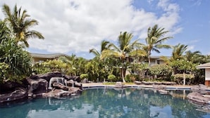 A pool surrounded by palm trees and rocks, with a clear sky. - You're Resort Home! Walk to Disney, Beach & Pool! (Kapolei)