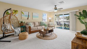 A living room with a sofa, coffee table, hanging chair, and a view of the outside. - You're Resort Home! Walk to Disney, Beach & Pool! (Kapolei)