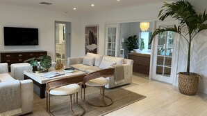 A modern living room with a sofa, armchairs, a coffee table, and a TV. There is a large plant and a wicker chair. - Modern Abode 3 miles from beach  (Lake Worth Beach)