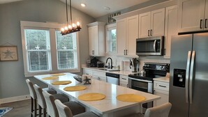 A modern kitchen with a central island, stainless steel appliances, and a dining area with bar stools. - Welcome to Saltwater Seaclusion! Heart of Corolla!  Walk to Everything! (Corolla)