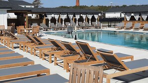 A poolside area with wooden lounge chairs and tables, a clear sky, and a distant lighthouse. - Welcome to Saltwater Seaclusion! Heart of Corolla!  Walk to Everything! (Corolla)