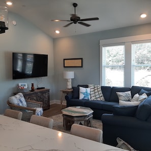 A living room with a blue couch, a television, a ceiling fan, and a window with blinds.