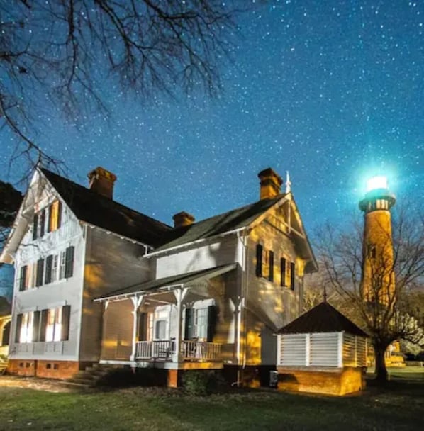 A two-story house with a porch and a lighthouse in the background.