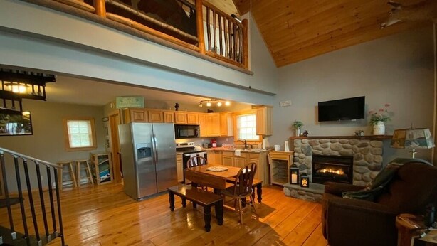 A spacious living area with a wooden floor, a dining table, a fireplace, and a kitchen with wooden cabinets and appliances.