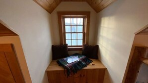 A small, cozy room with a sloped ceiling, a window with blinds, and a bench with cushions.