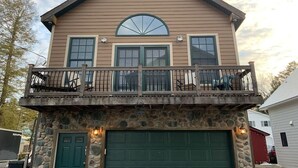 A two-story house with a stone foundation, a green garage door, and a balcony with outdoor furniture.