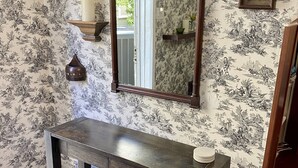 Una habitación con una mesa de madera oscura, dos taburetes, un espejo y estantes en la pared con objetos decorativos.