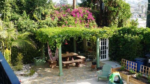 Un patio con pérgola, suelo de piedra, una mesa de madera, un banco y un pequeño coche de juguete verde.