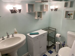 Un baño con lavamanos, inodoro y repisas con artículos de aseo.