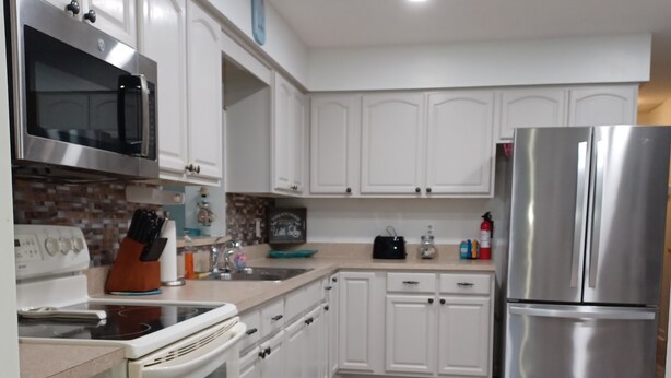 A modern kitchen with white cabinets, stainless steel appliances, and a blue mat on the floor. - Cozy canal front home. Minutes from Sebring International Raceway. (Lake Placid)