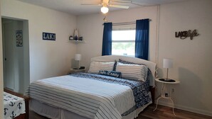 A neatly arranged bedroom with a bed, bedside lamps, a ceiling fan, a window with curtains, and a wall sign. - Cozy canal front home. Minutes from Sebring International Raceway. (Lake Placid)